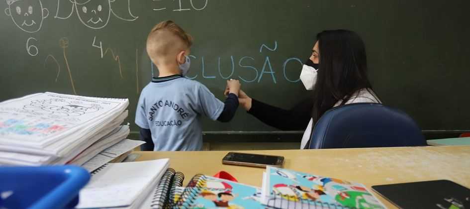 Criança portadora de deficiência escrevendo na lousa a palavra 'Inclusão'